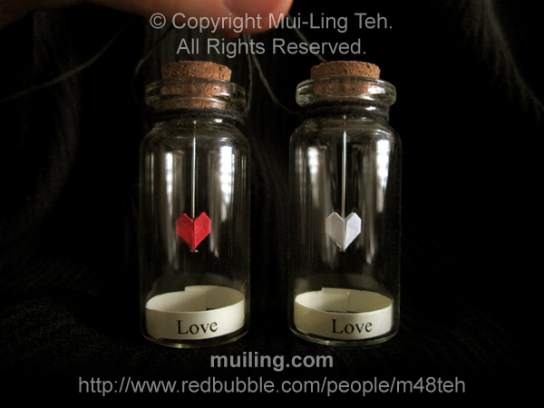 Miniature red and white origami hearts by Mui-Ling Teh, hanging on needles in a bottle; with the word 'Lov' written on yellow labels