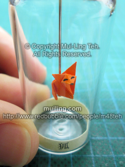 A cute miniature orange origami fox in a bottlle, with a yellow label saying "fox" in Japanese.