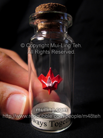 Miniture red origami crane and maple leaf in a bottle by Mui-Ling Teh, with the message "Always Together" written below on a yellow label. Origami design by Mui-Ling Teh. The crane and the leaf are made out of one paper.