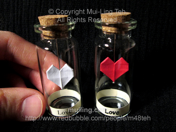 red and white miniature origami hearts by Mui-Ling Teh, hanging on needles in a bottle; with the word 'Love' written on a yellow label