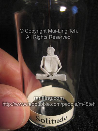 Miniature origami meditation figure in a bottle, with the word 'Solitude' on a yellow label