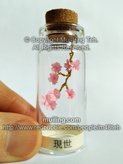 Hand coloured miniature pink and white origami hydrangea flower in a bottle with the word "Hope" at the bottom.