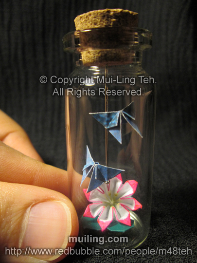 Bottled hand-coloured pink origami flower with two blue origami butterlflies by Mui-Ling Teh