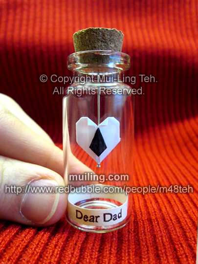 white miniature origami heart with a black necktie by Mui-Ling Teh, hanging on a needle in a bottle, with the words 'Dear Dad' on a yellow label